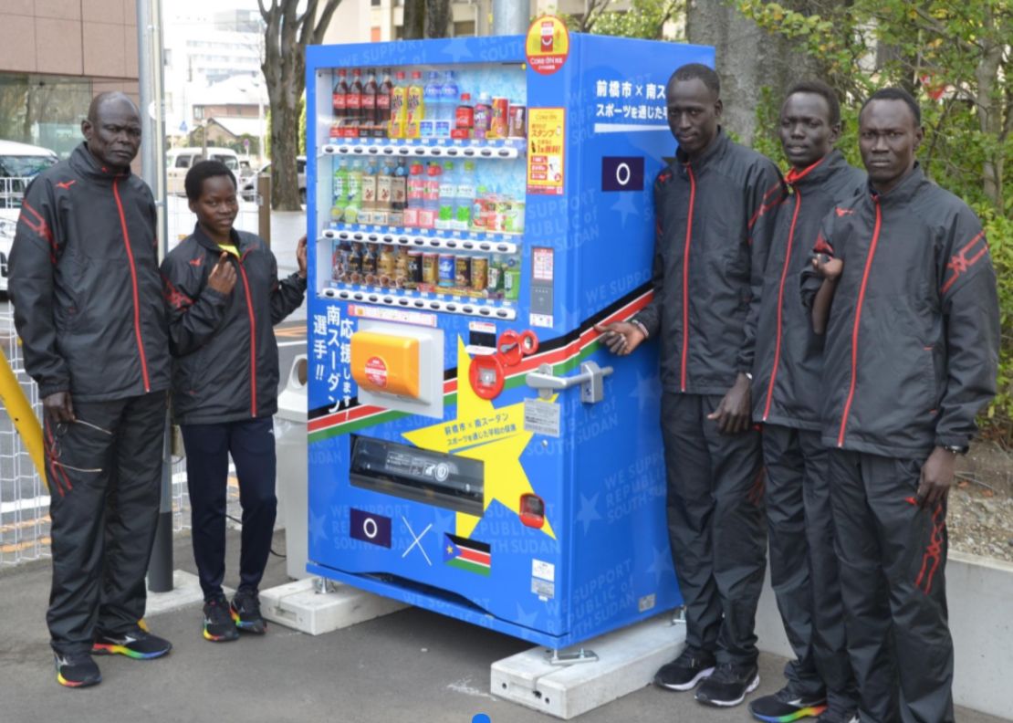 The South Sudan team and their coach, Joseph, (far left) in front of a vending machine in Maebashi city, displaying their nation's flag. 