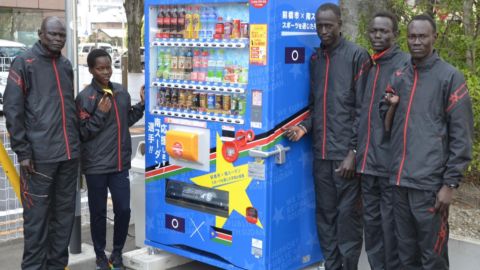 The South Sudan team and their coach, Joseph, (far left) in front of a vending machine in Maebashi city, displaying their nation's flag.