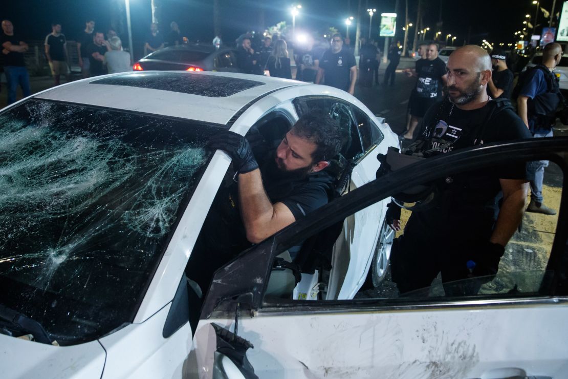 An Israeli police officer inspects the car of an Israeli Arab man who was attacked and injured by a mob Wednesday in Bat Yam, Israel.