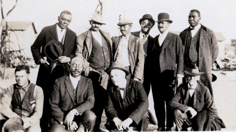 Originally from Arkansas, businessman <strong>Ottawa W. Gurley</strong> (front row, second from left) moved to Tulsa circa 1905 and bought 40 acres of land that he subdivided and sold to Black buyers. That, <a href="index.php?page=&url=http%3A%2F%2Fblackwallstreet.org%2Fowgurley" target="_blank" target="_blank">followed by a grocery store and rooming house</a> that he built, helped enable other entrepreneurial Tulsans to move to the community and open up shop in Greenwood. 