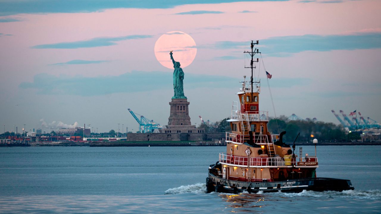 The lovely flower moon from 2020 looms over the Statue of Liberty in New York Harbor.