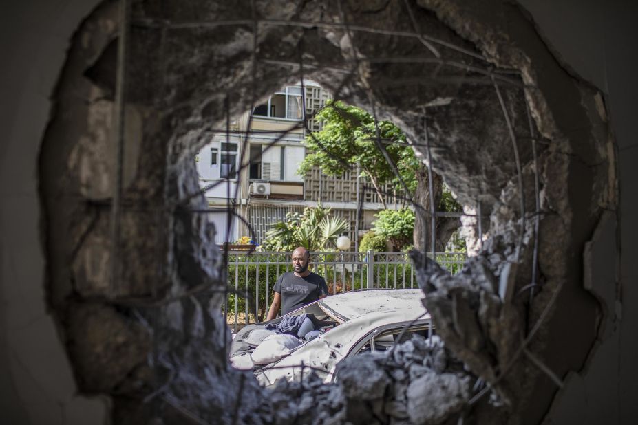 A man in Ashkelon, Israel, views a damaged car and building that was hit by a rocket fired from Gaza.