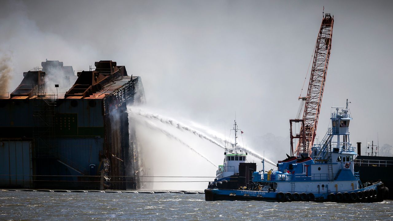 Firefighters working off two tug boats hose down the remains of the overturned cargo ship.