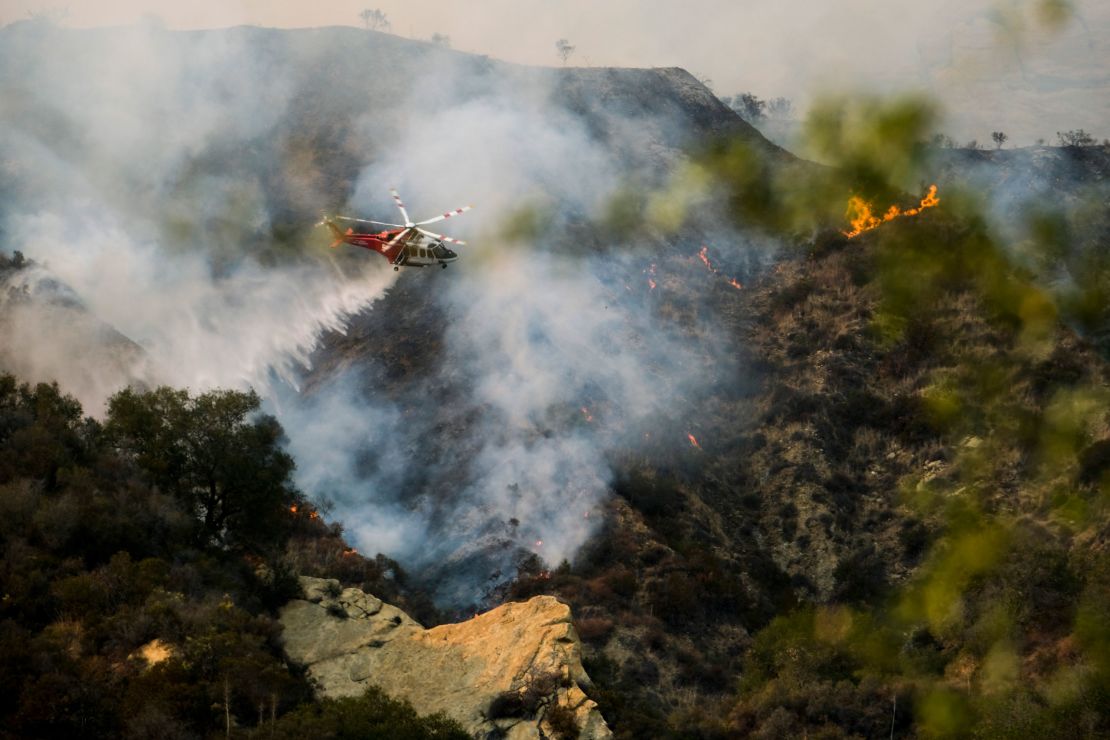 A firefighting helicopter drops water on a brush fire scorching of an area west of Los Angeles Saturday, May 15, 2021. 