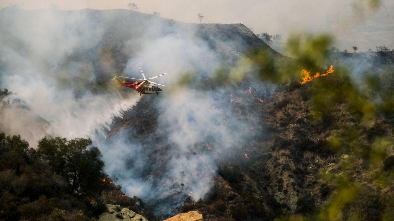 A firefighting helicopter drops water on a brush fire scorching of an area west of Los Angeles Saturday, May 15, 2021.