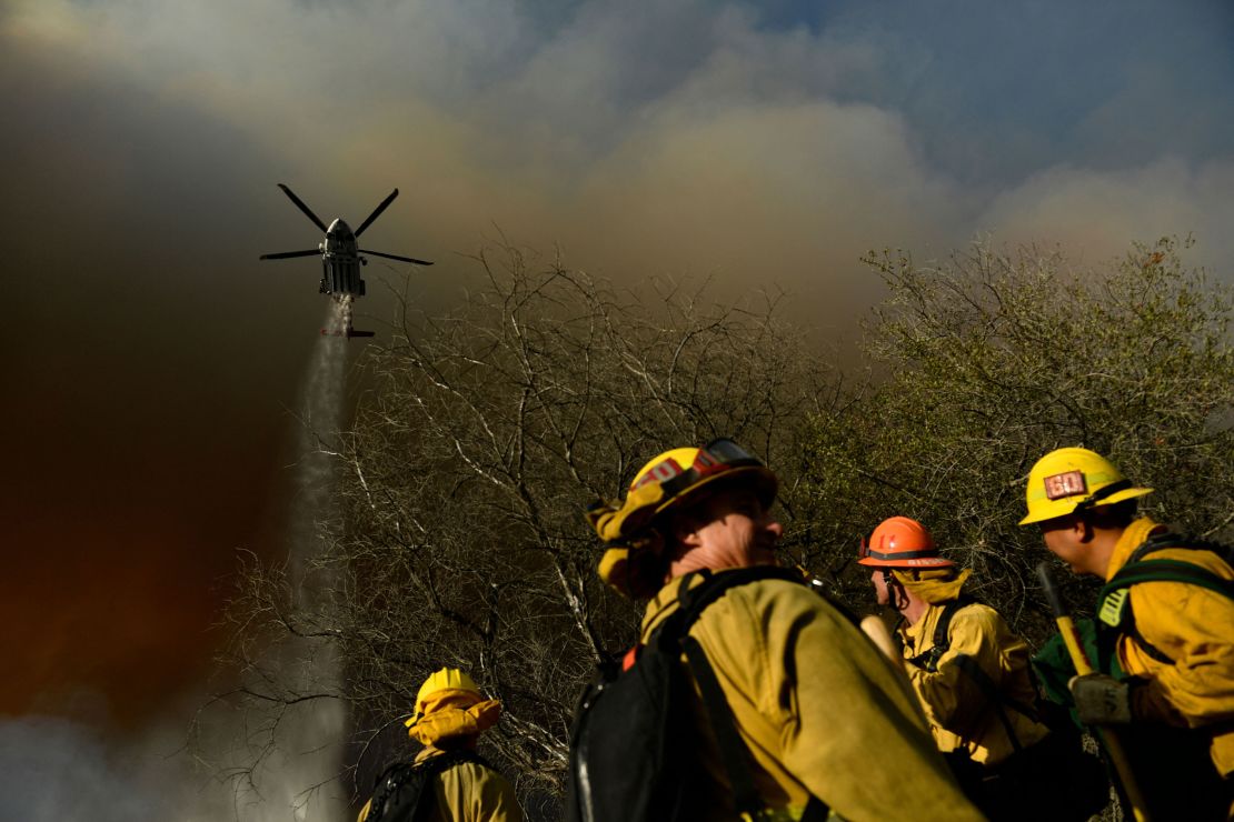 Firefighters keep a lookout as a Los Angeles Fire Department helicopter makes a water drop on the Palisades fire in Topanga State Park, North West of Los Angeles on May 15, 2021.