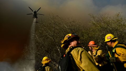 Firefighters keep a lookout as a Los Angeles Fire Department helicopter makes a water drop on the Palisades fire in Topanga State Park, North West of Los Angeles on May 15, 2021.