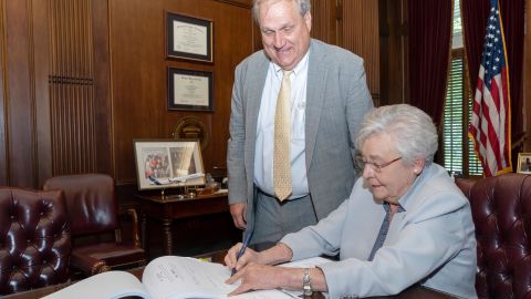 Governor Kay Ivey signs a bill legalizing medical marijuana in Alabama as State Sen. Tim Melson looks on.