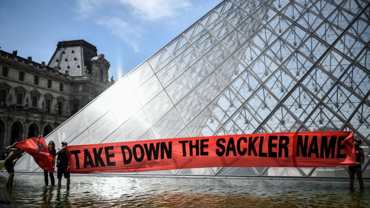Activists hold a banner reading "Take down the Sackler name" in front of the Pyramid of the Louvre on July 1, 2019. Shortly thereafter, the Louvre removed the name of the Sackler family from its walls, becoming the first major museum to remove its association with the Sackler family. 