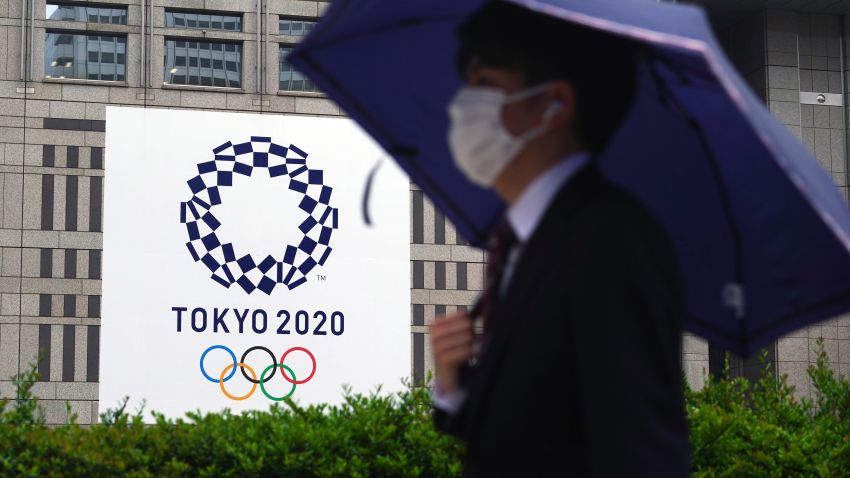 A man wearing a protective mask to help curb the spread of the coronavirus walks in the rain past a banner of Tokyo 2020 Olympic Games Thursday, May 13, 2021, in Tokyo. The Japanese capital confirmed more than 1,000 new coronavirus cases on Thursday. (AP Photo/Eugene Hoshiko)