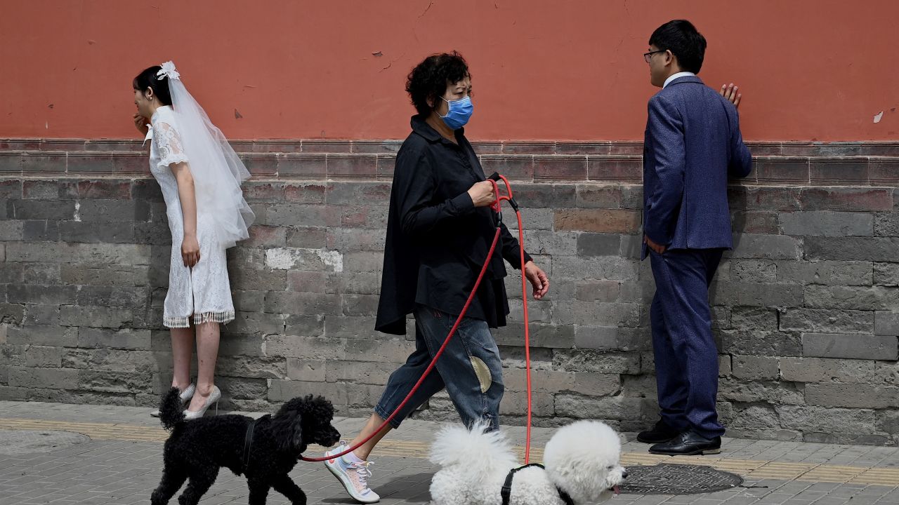 A woman walks her dogs past a couple posing for wedding photographs in Beijing on May 16, 2021.