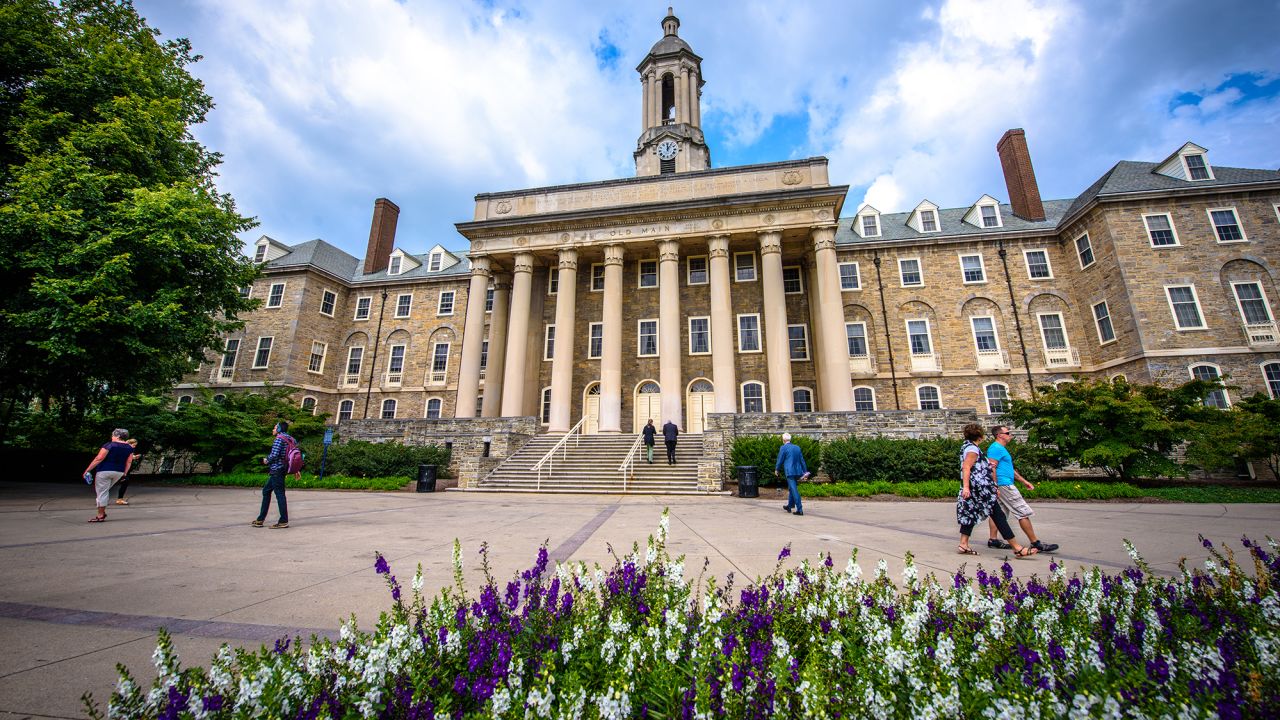 Students and adults walk in front of the Old Main building, on the campus of Penn State University, in State College, Pennsylvania. 