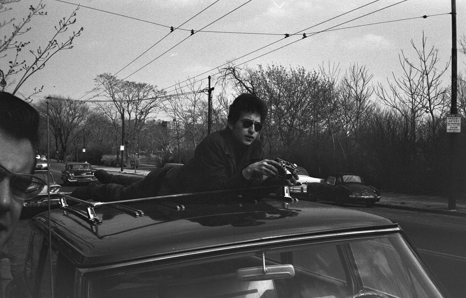 Dylan holds a camera on the top of a car in Massachusetts in 1964.