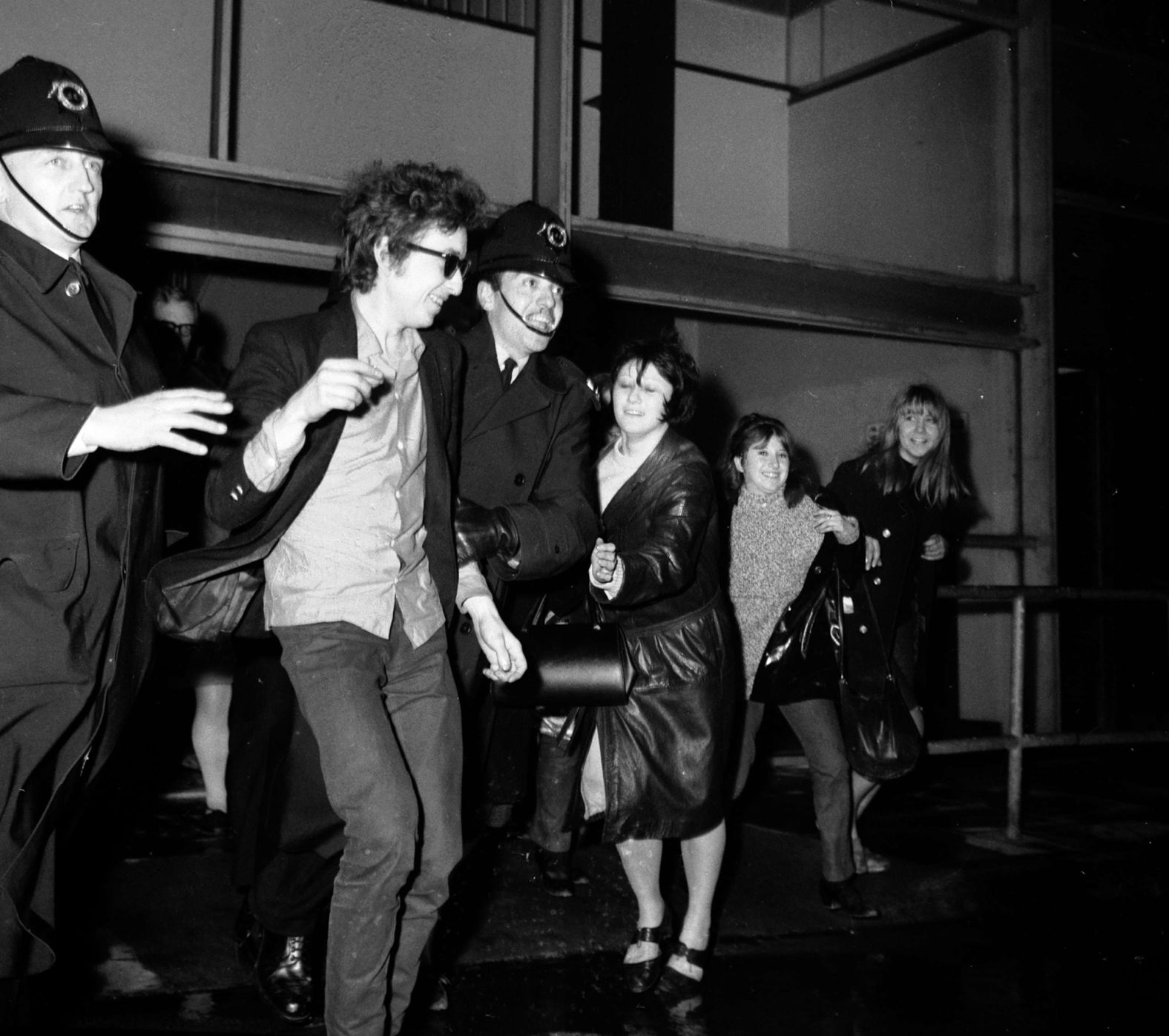 Dylan is escorted past fans as he arrives at a London airport in 1965.