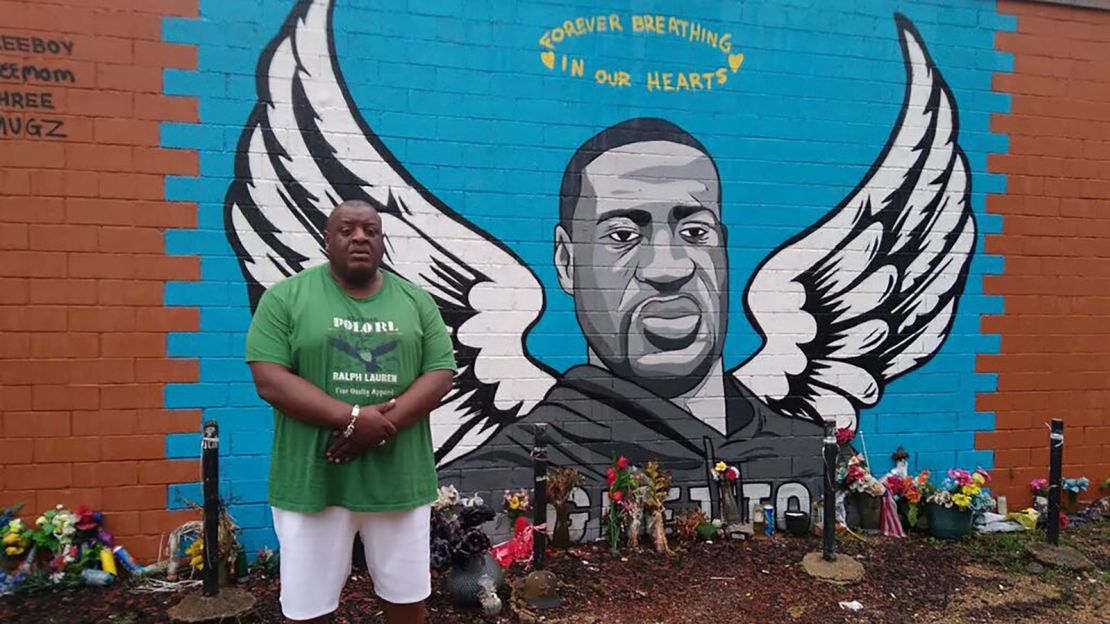 Travis Cains stands alongside a George Floyd mural.