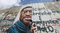 People walk past a mural showing the face of George Floyd, an unarmed handcuffed black man who died after a white policeman knelt on his neck during an arrest in the US, painted on a section of Israel's controversial separation barrier in the city of Bethlehem in the occupied West Bank on March 31, 2021. - The teenager who took the viral video of George Floyd's death said on March 30, at the trial of the white police officer charged with killing the 46-year-old Black man that she knew at the time "it wasn't right." Darnella Frazier, 18, was among the witnesses who gave emotional testimony on Tuesday at the high-profile trial of former Minneapolis police officer Derek Chauvin. Chauvin, 45, is charged with murder and manslaughter for his role in Floyd's May 25, 2020 death, which was captured on video by Frazier and seen by millions, sparking anti-racism protests around the globe. In the video, Chauvin, who was subsequently fired from the police department, is seen kneeling on the neck of a handcuffed Floyd for more than nine minutes. (Photo by Emmanuel DUNAND / AFP) (Photo by EMMANUEL DUNAND/AFP via Getty Images)