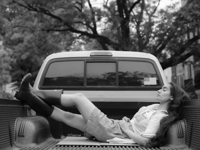 One of Kung's models sits in the back of a pickup truck in fishing boots.