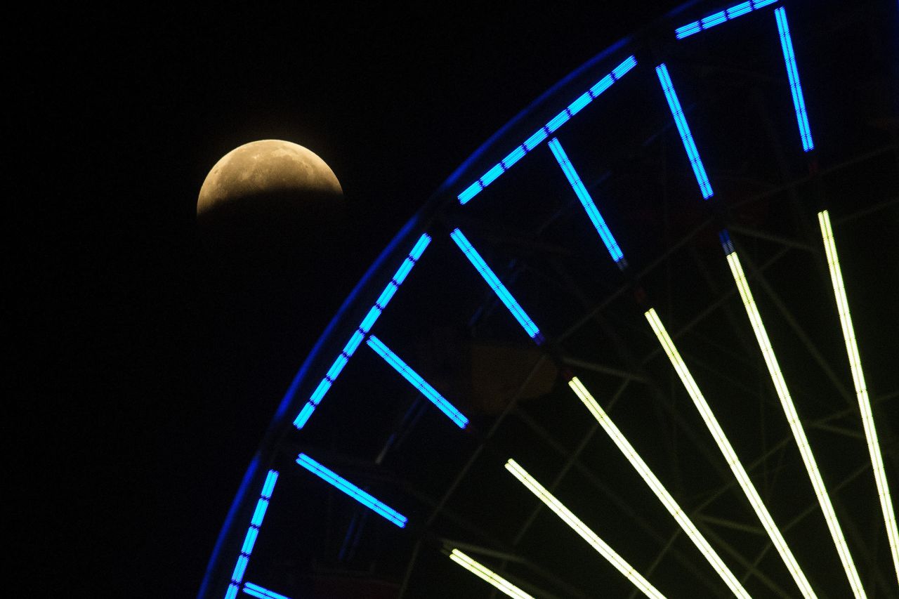 The lunar eclipse is seen behind a Ferris wheel in Santa Monica, California.