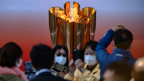 TOPSHOT - People wearing face masks take pictures in front of the Tokyo 2020 Olympic flame, which is displayed outside Sendai railway station, Miyagi prefecture on March 21, 2020, after arriving from Greece. (Photo by Philip FONG / AFP) (Photo by PHILIP FONG/AFP via Getty Images)