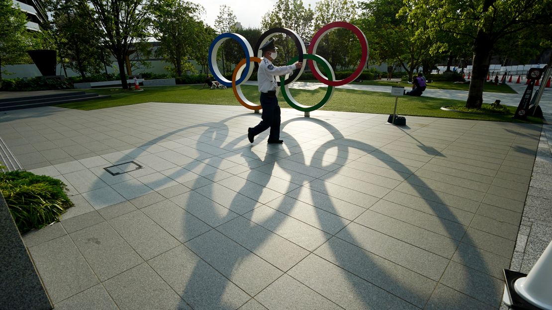 A masked guard walks in front of the Olympic Rings in Tokyo in May 2021.