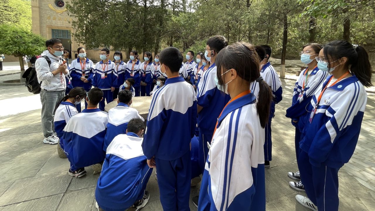 Students in school uniforms receive an open-air lecture on the Communist Party's early days in front of a historical building in Yan'an.