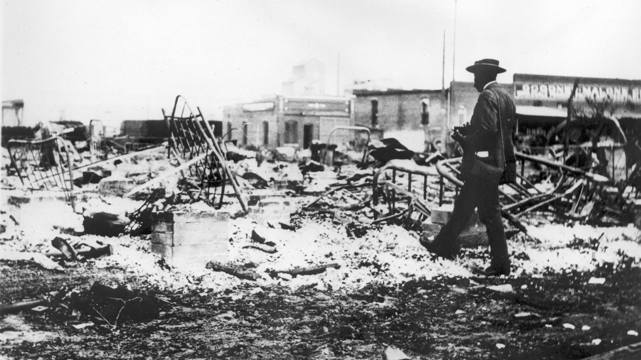 An African-American man with a camera looking at the skeletons of iron beds which rise above the ashes of a burned-out block after the Tulsa Race Massacre, Tulsa, Oklahoma, June 1921. (Photo by Oklahoma Historical Society/Getty Images)