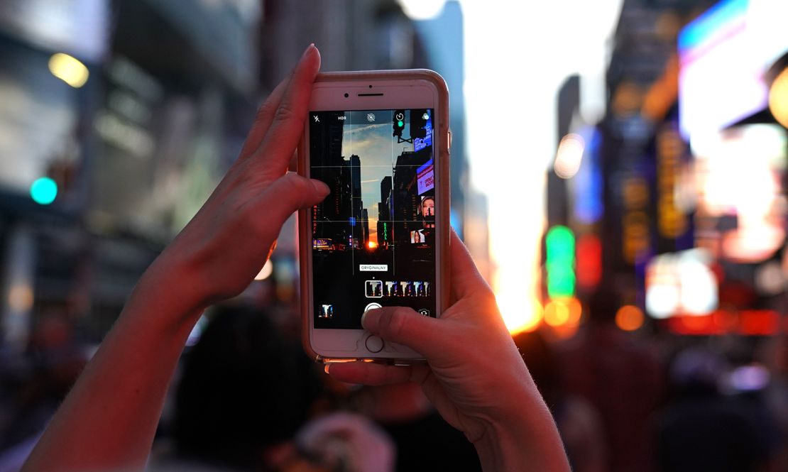 A woman takes a photo with her mobile phone as the sun sets on Times Square in New York City on July 12, 2018, during Manhattanhenge.