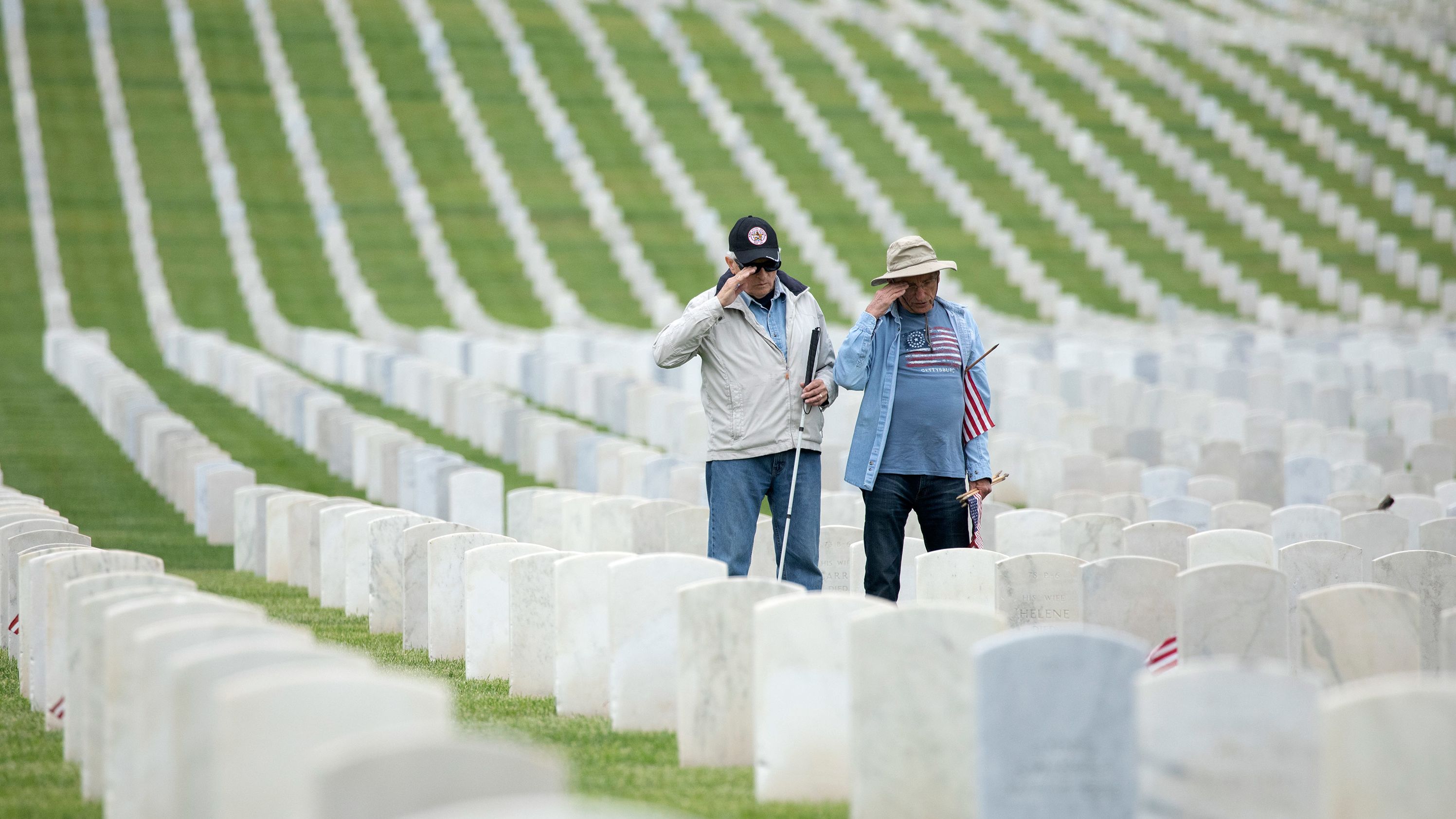 Air Force veteran Larry Bustetter, left, and Army veteran Henry Knebel salute after placing flags at the Los Angeles National Cemetery on Saturday.