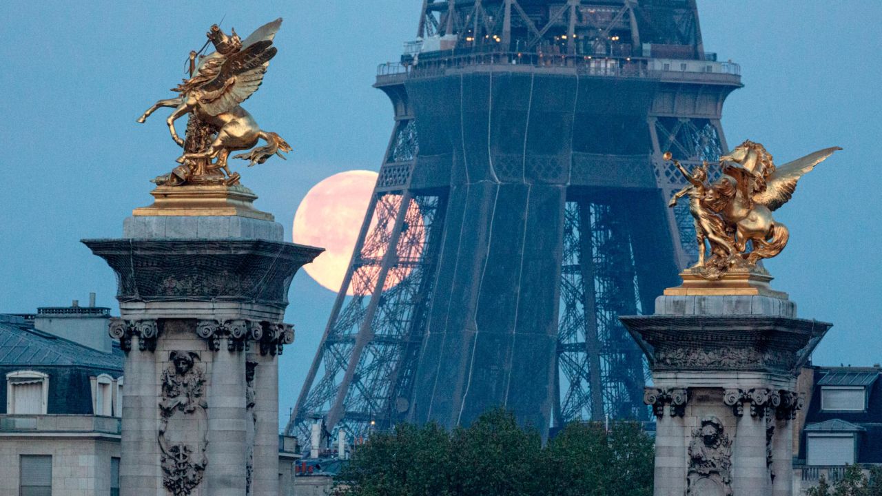 A supermoon sets behind the Eiffel Tower and statues of Pegasus Held By Fame on the Pont Alexandre III bridge in Paris on April 27, 2021.