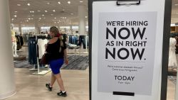 A customer walks behind a sign at a Nordstrom store seeking employees, Friday, May 21, 2021, in Coral Gables, Fla.  The number of Americans seeking unemployment benefits dropped last week to 406,000, a new pandemic low and more evidence that the job market is strengthening as the virus wanes and economy further reopens. (AP Photo/Marta Lavandier)