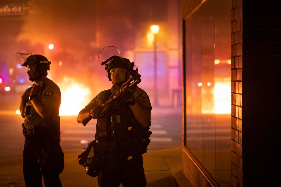 Police stand guard early Saturday after protesters set fire to trash bins in Minneapolis.