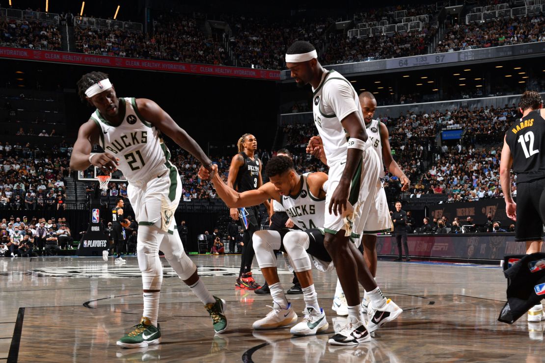 Jrue Holiday and Bobby Portis of the Bucks help up Antetokounmpo during their game against the Nets.