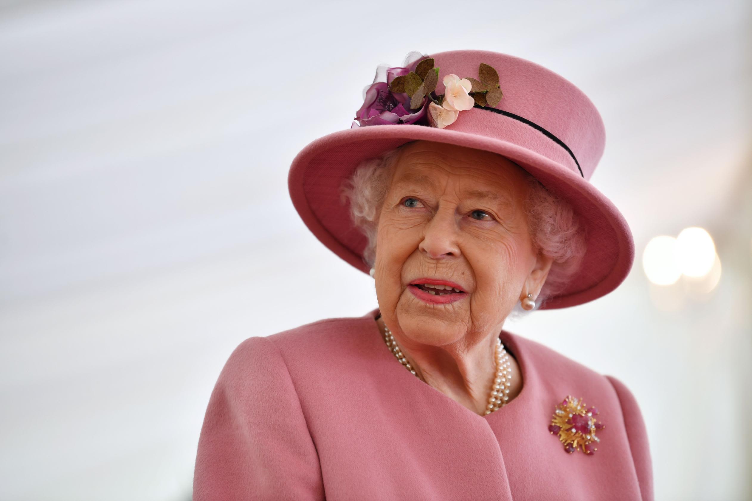 The Queen of England in a pink outfit with pearls and gorgeous hat.
