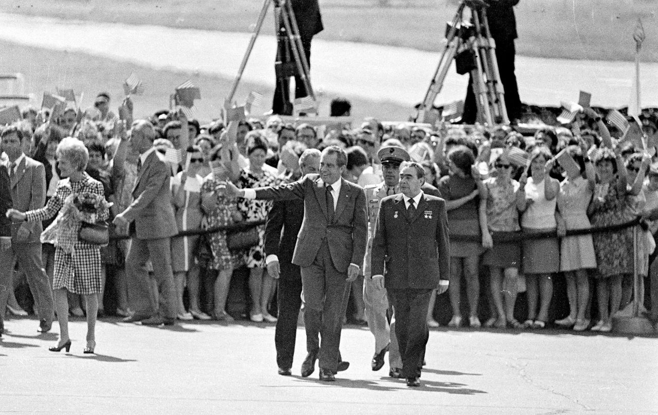 Nixon, escorted by Brezhnev, waves to embassy staff members and families after arriving in Moscow in 1974. At left is first lady Pat Nixon.