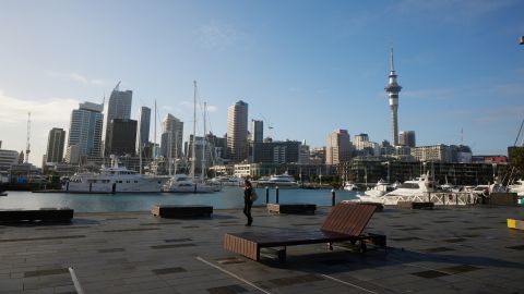 A pedestrian walks past a marina as the Sky Tower and other buildings stand in the background in Auckland, New Zealand, on Wednesday, Sept. 16, 2020. New Zealands economy will endure a shallower recession than previously expected but the coronavirus pandemic will have a longer impact on the countrys finances, according to government projections. Photographer: Brendon O'Hagan/Bloomberg via Getty Images