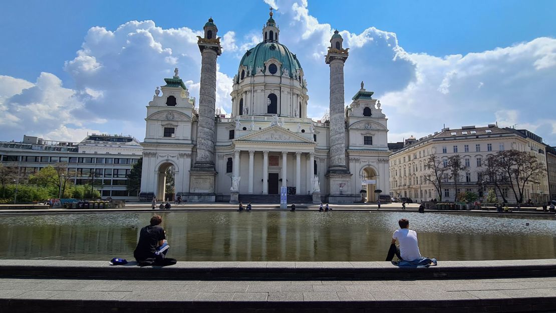 People rest at a fountain in front of the Karlskirche in Vienna, Austria.