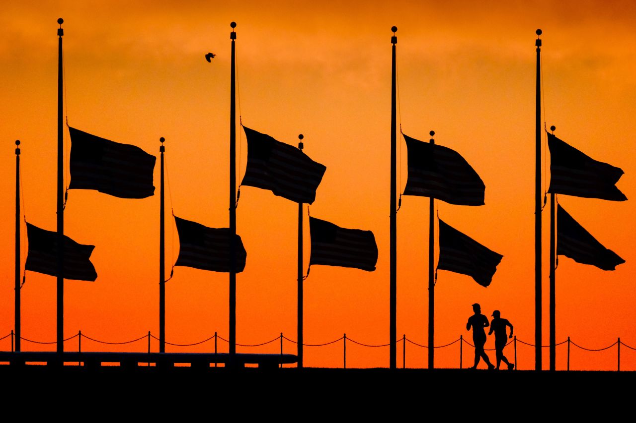 The day after the shooting, runners pass under flags flying at half-staff around the Washington Monument.