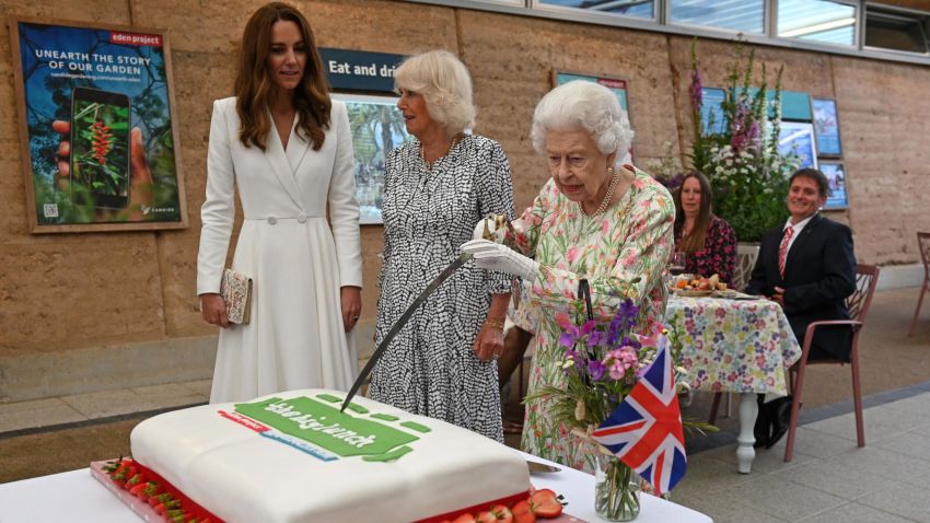 TOPSHOT - Britain's Queen Elizabeth II (C) attempts to cut a cake with a sword, lent to her by The Lord-Lieutenant of Cornwall, Edward Bolitho, to celebrate of The Big Lunch initiative at The Eden Project, near St Austell in south west England on June 11, 2021. (Photo by Oli SCARFF / POOL / AFP) (Photo by OLI SCARFF/POOL/AFP via Getty Images)