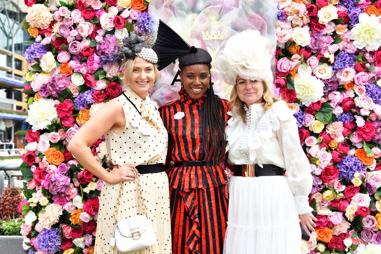 Three attendees showcase their headgear in front of a giant flower wall.