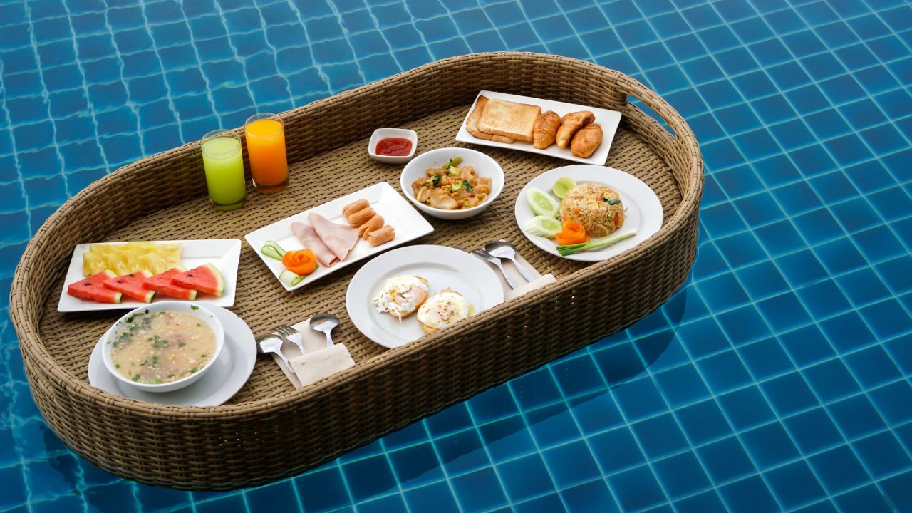 Breakfast in swimming pool, floating breakfast in tropical resort. Breakfast in a wicker tray right on the water surface of the pool.Beautiful cozy luxury breakfast for two at the private pool. 