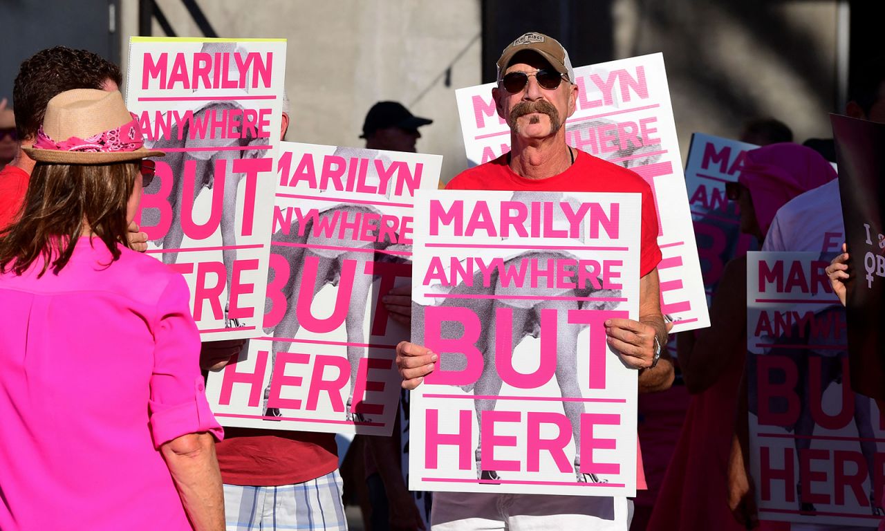 Protestors hold up signs at the unveiling of the "Forever Marilyn" sculpture.
