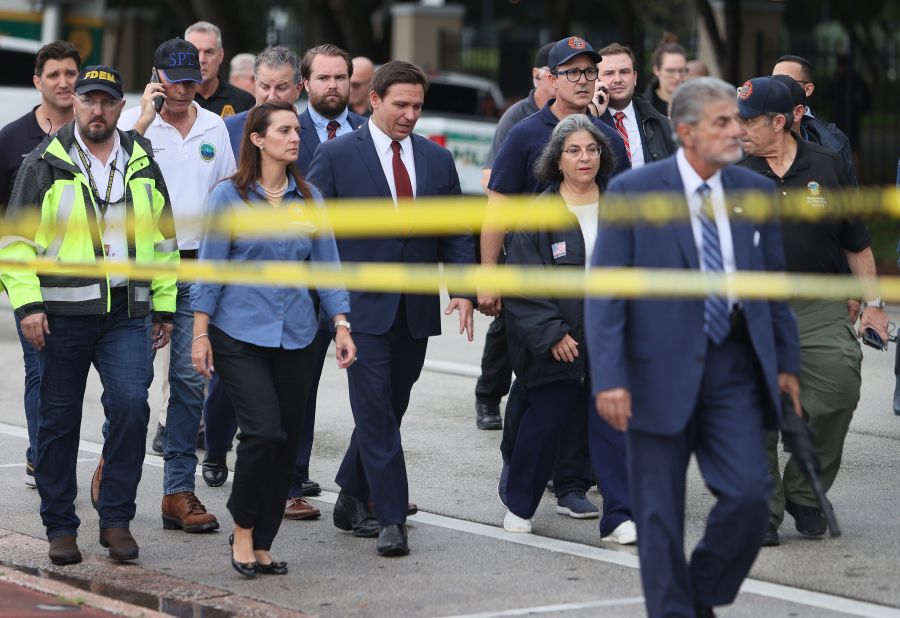 Florida Gov. Ron DeSantis, at center in the red tie, arrives to speak to the media on June 24. "We still have hope to be able to identify additional survivors," DeSantis told reporters near the scene. "The state of Florida, we're offering any assistance that we can."