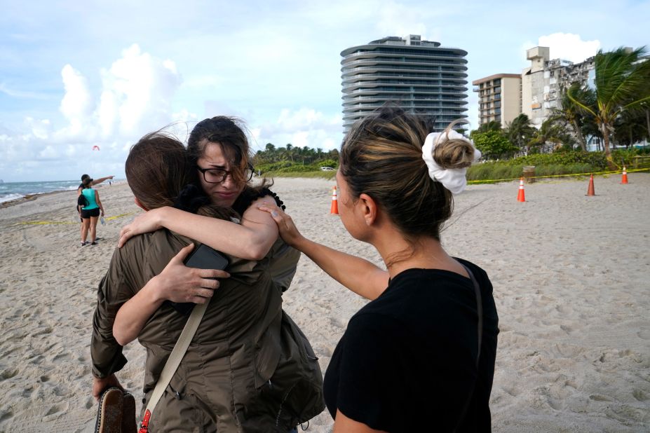 Faydah Bushnaq, center, is hugged by Maria Fernanda Martinez as they stand on the beach near the building. Bushnaq, who was vacationing in South Florida, stopped to write "pray for their souls" in the sand.