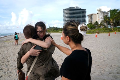 Faydah Bushnaq, center, is hugged by Maria Fernanda Martinez as they stand on the beach near the building. Bushnaq, who was vacationing in South Florida, stopped to write 