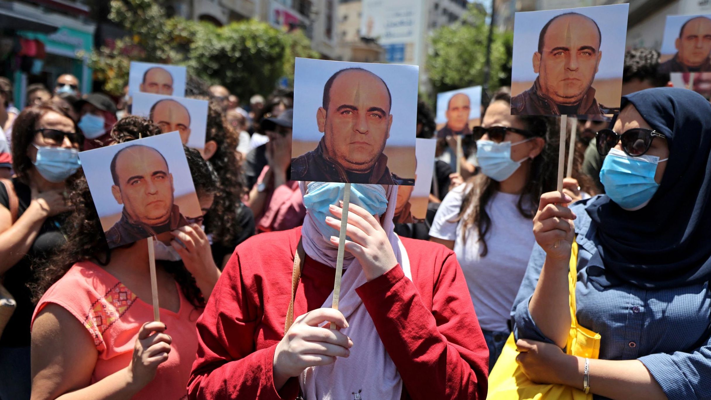 Protestors hold images of Palestinian activist Nizar Banat, who died while in the custody of PA security forces on Thursday morning.
