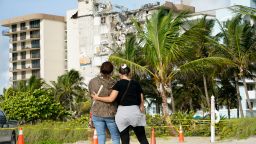Maria Fernanda Martinez, left, and Mariana Corderiro, right, of Boca Raton, Fla., stand outside of a 12-story beachfront condo building which partially collapsed, Friday, June 25, 2021, in the Surfside area of Miami.   The apartment building partially collapsed on Thursday.(AP Photo/Lynne Sladky)
