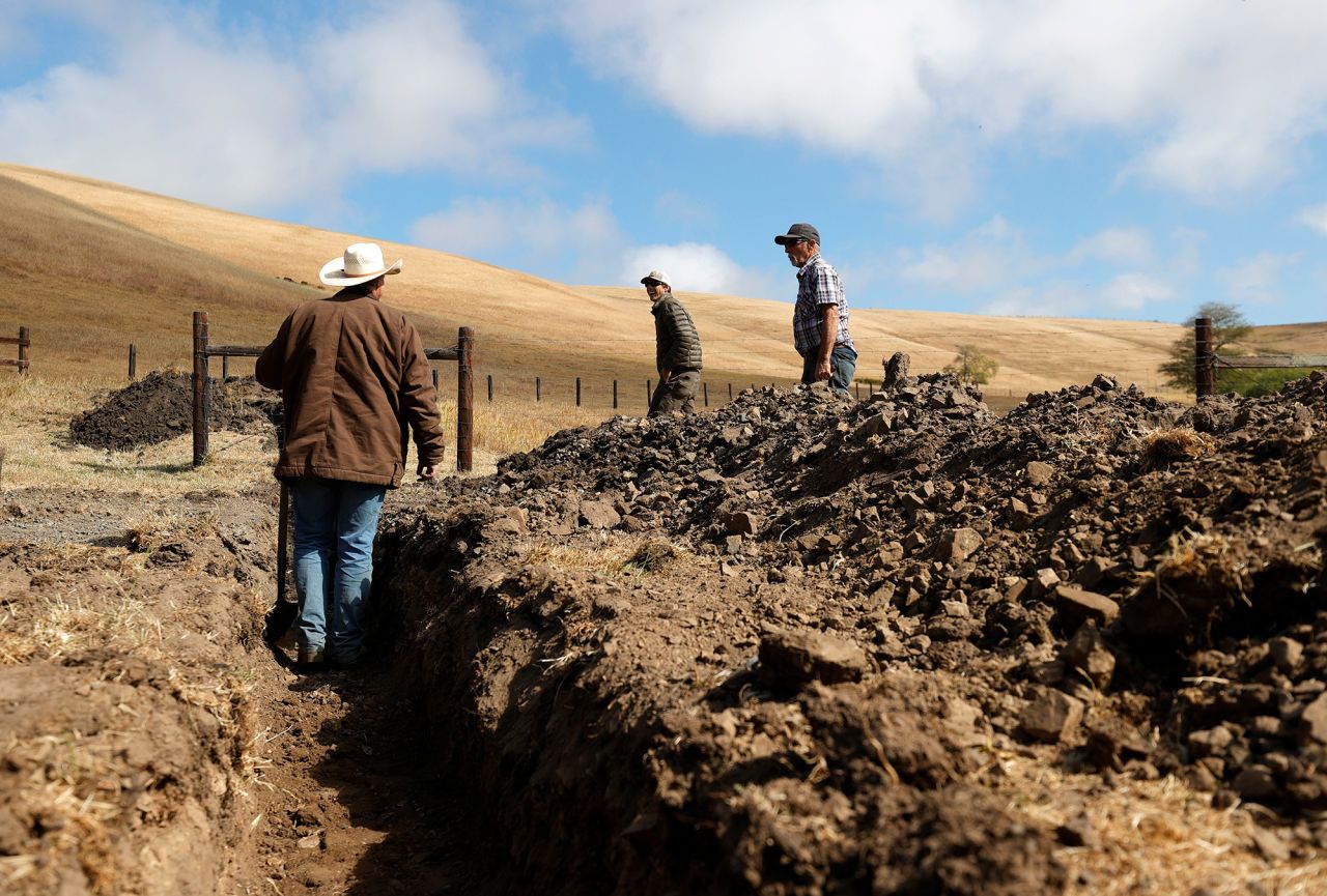 Ranchers Jim Jensen, center, and Bill Jensen inspect a trench they are working on to try to get more water to their ranch in Tomales, California, in June 2021. As the drought continues in California, many ranchers and farmers are beginning to see their wells and ponds dry up. They are having to make modifications to their existing water resources or have water trucked in for their livestock.