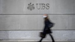 A pedestrian wearing a facemask as a preventive measure against Covid-19 walks by the logo of Swiss banking giant UBS engraved on the wall of its headquarters in Zurich on March 3, 2021.