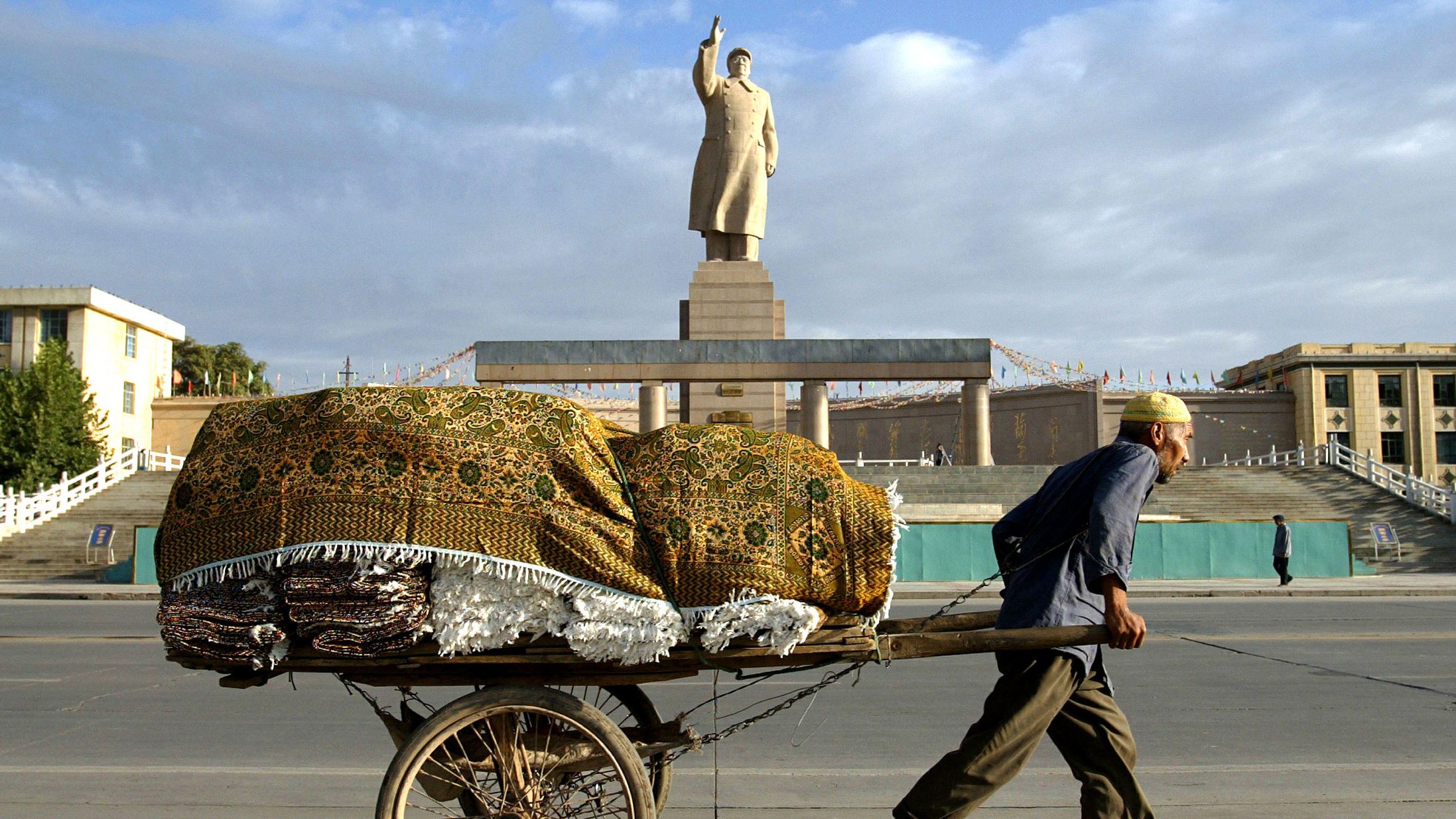 A Uyghur worker pulls a cart past a giant Mao statue at the People's Square in Kashgar, China, in September 2003.