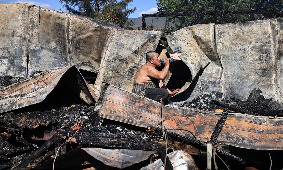 Carlos Torres hydrates, even as ashes have not yet cooled at his mobile home of 22 years, as he was looking for paperwork during the aftermath of a fire in Kelseyville, Calif., that burned three mobile homes, two separate garages and vehicles, a single family dwelling and outbuildings in a wind whipped brush fire that prompted tense moments and evacuations, amid temperatures well over 100 degrees, Saturday, June 26, 2021. 